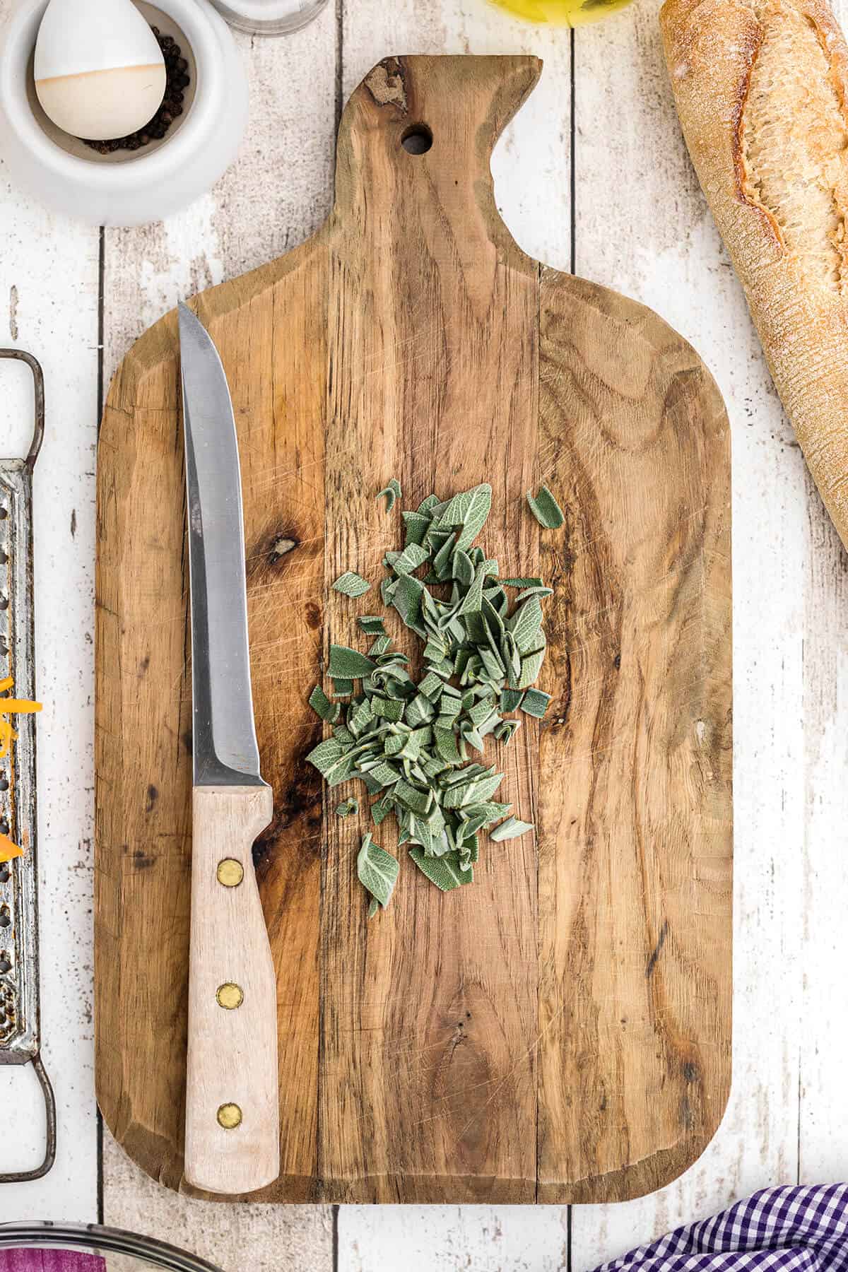Chopped fresh sage on a cutting board with a knife to the side.