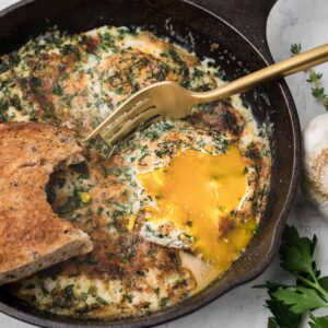 Finished baked eggs in a small skillet with a fork and toast.