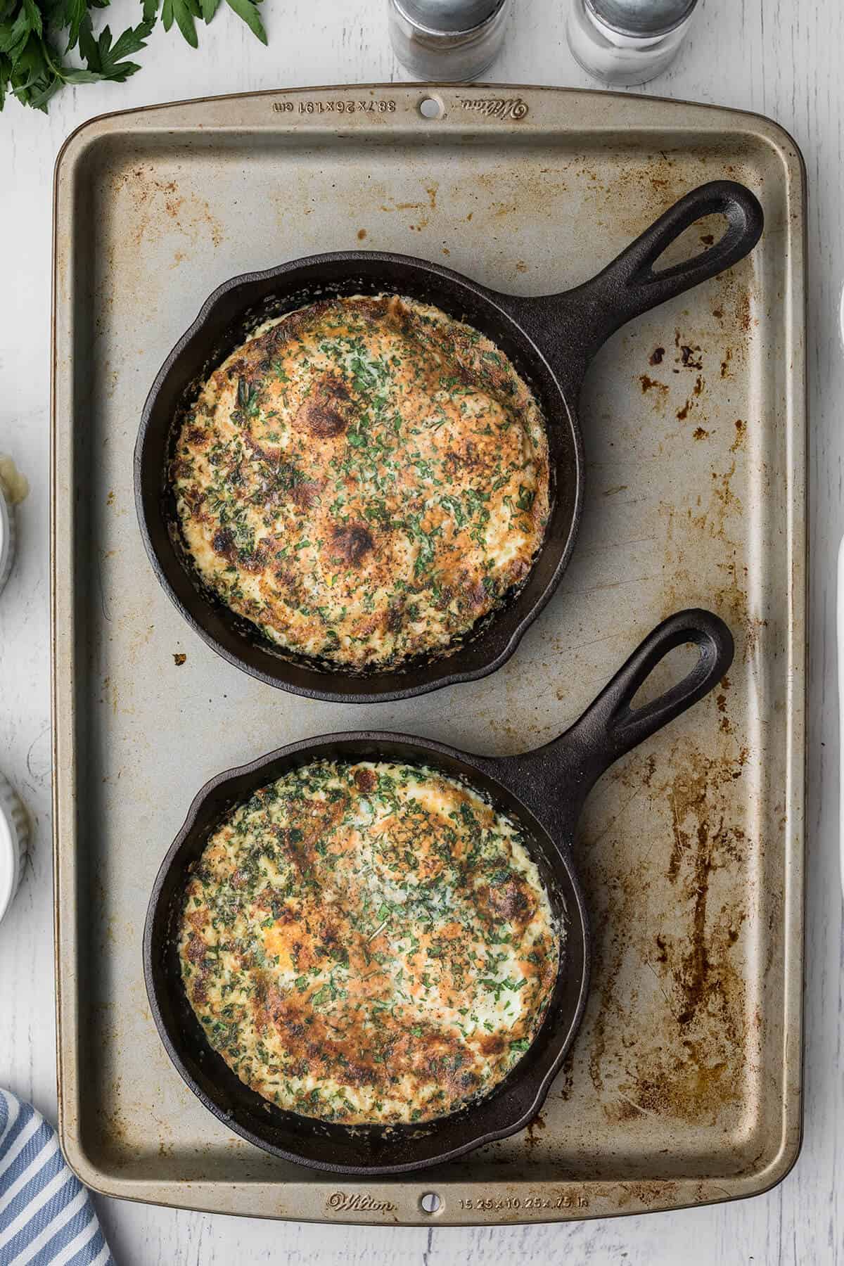 Finished eggs in skillets on a baking pan.