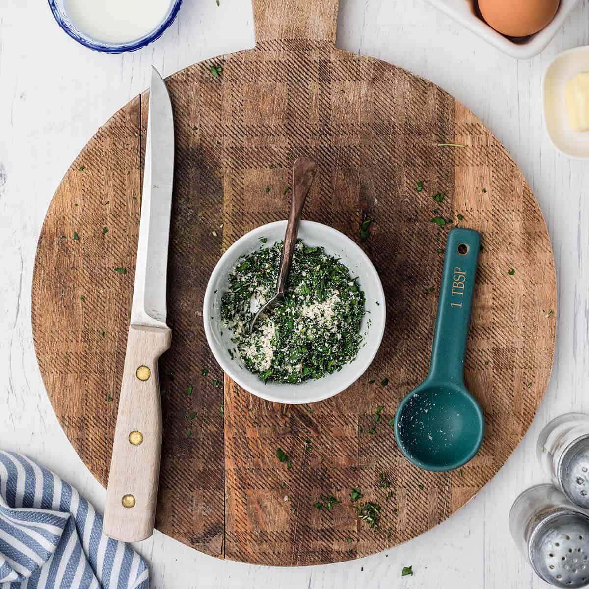 Herbs and garlic in a small bowl on a cutting board.