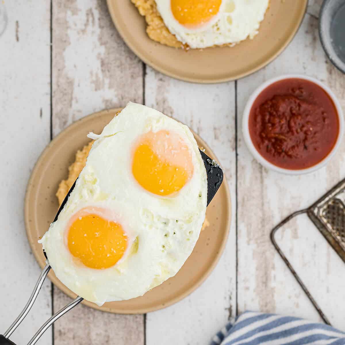 Adding fried eggs on top of cheese grits on a serving plate.