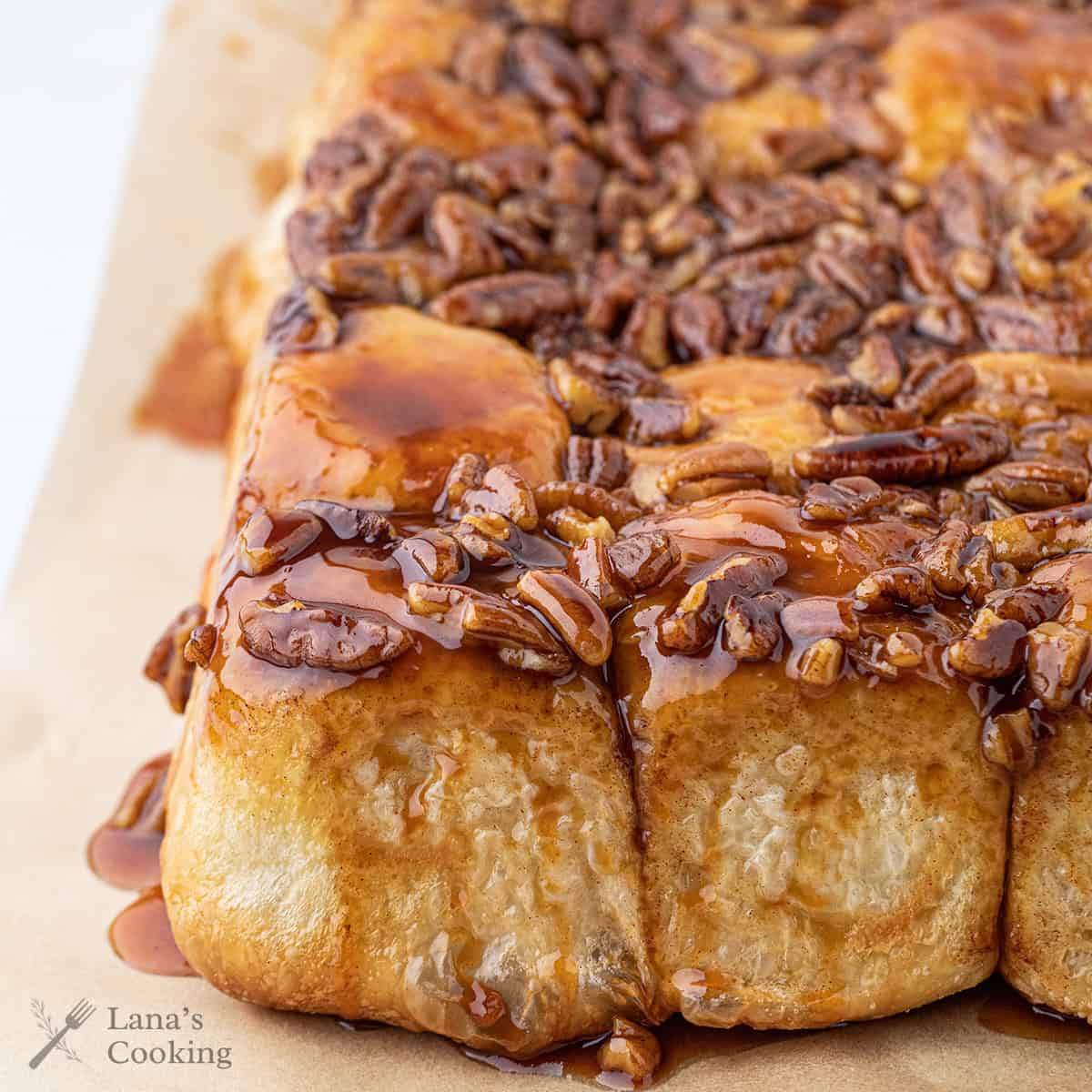 Sticky pecan cinnamon rolls topped with pecans and glaze, close-up view on parchment paper.