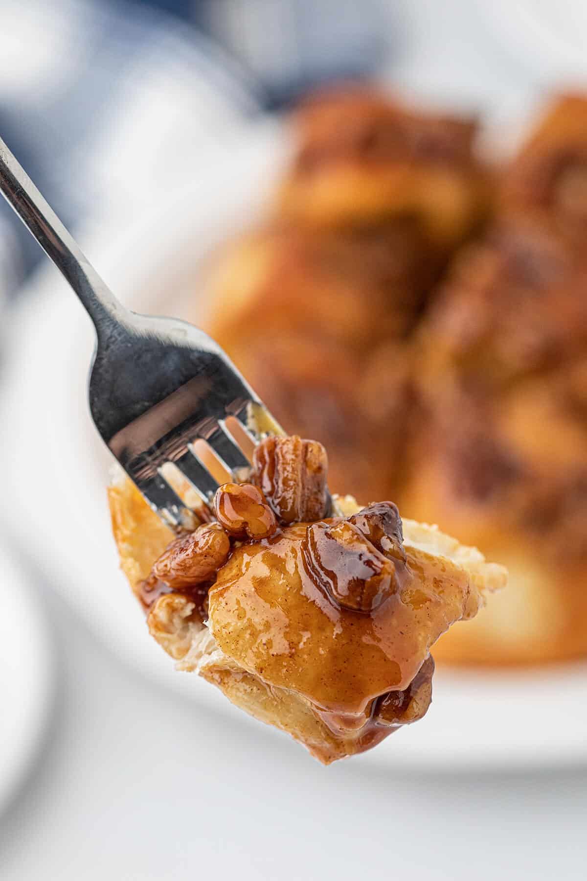 A fork holding one bite of a pecan sticky bun.