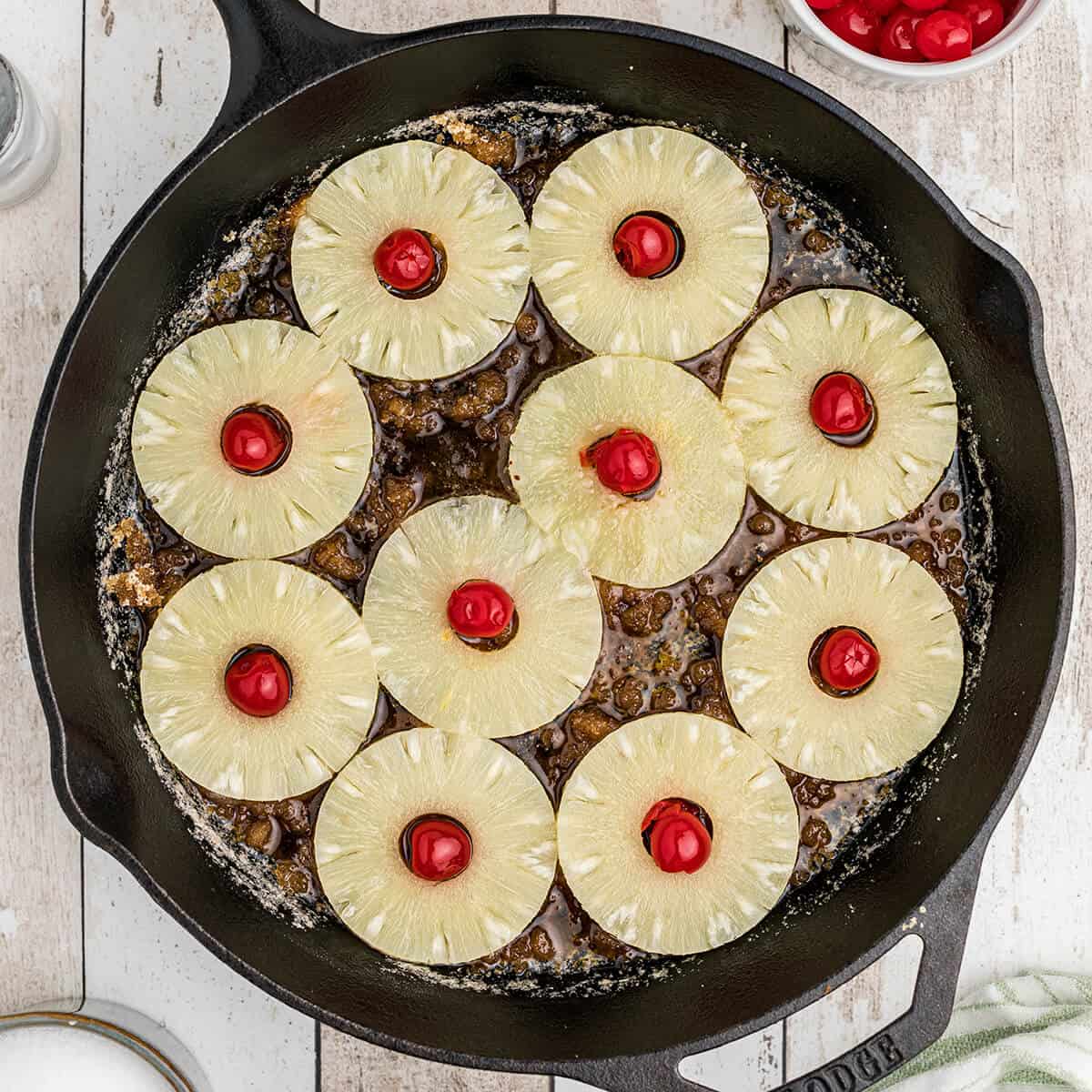 Cherries placed in the center of pineapple rings in a skillet.