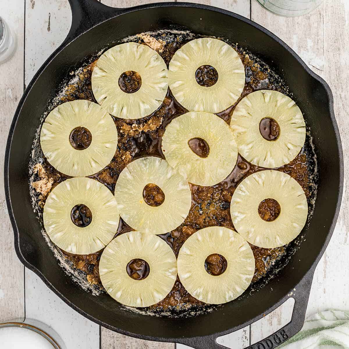 Pineapple slices placed over brown sugar and butter in a cast iron skillet.