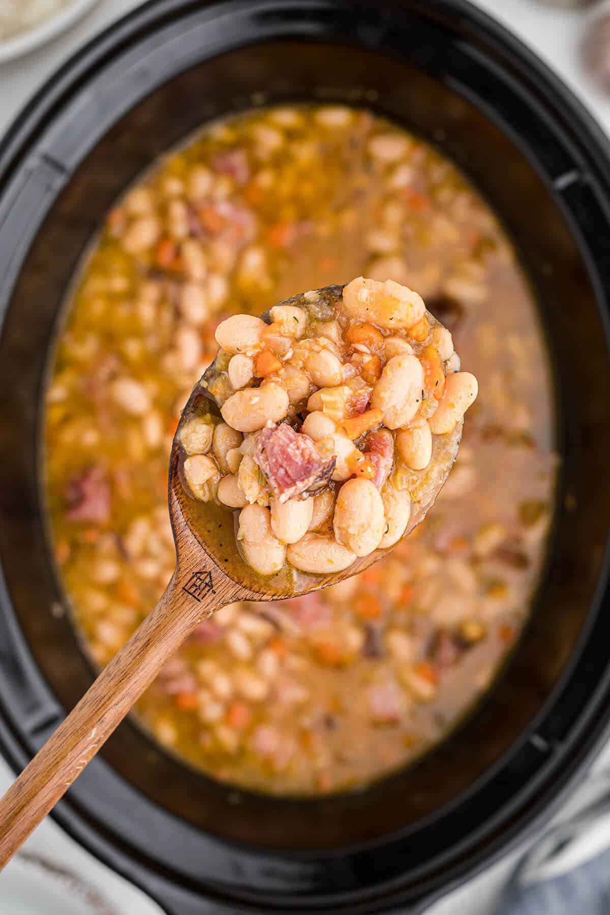 A spoonful of white beans held over a slow cooker.