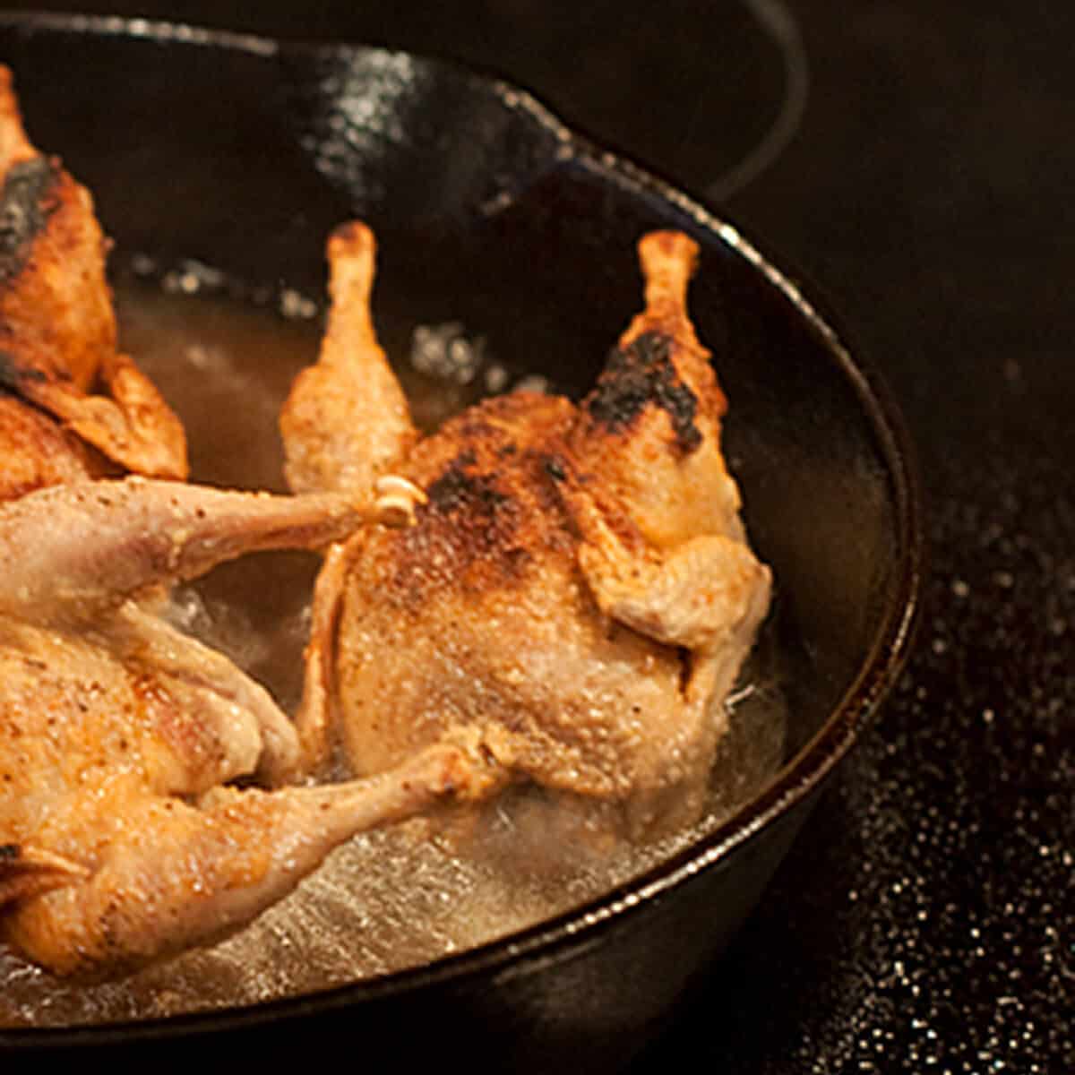 Quail frying in a cast iron pan.