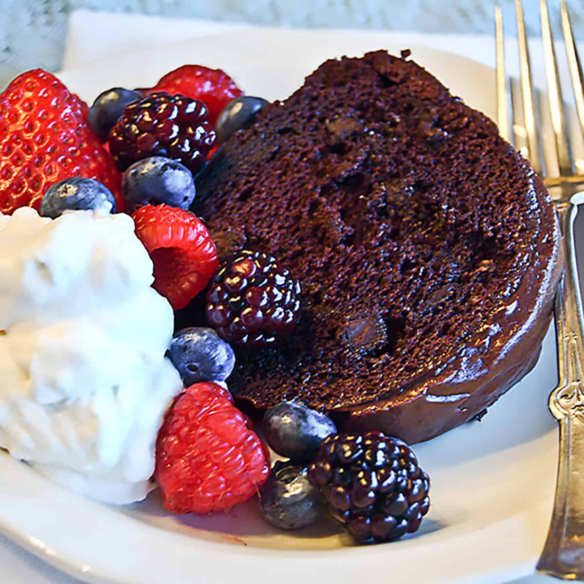 A serving of berry glazed chocolate cake with whipped cream.