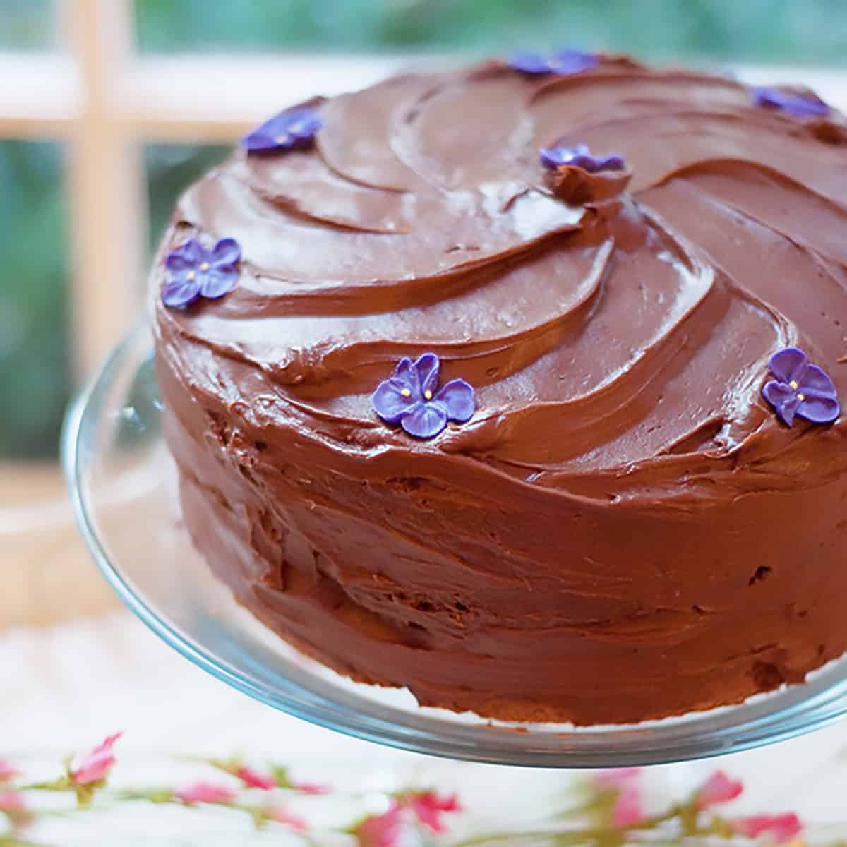 Chocolate cake with floral decorations on a glass pedestal.