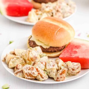 Southern potato salad on a white plate with a hamburger and slice of watermelon.