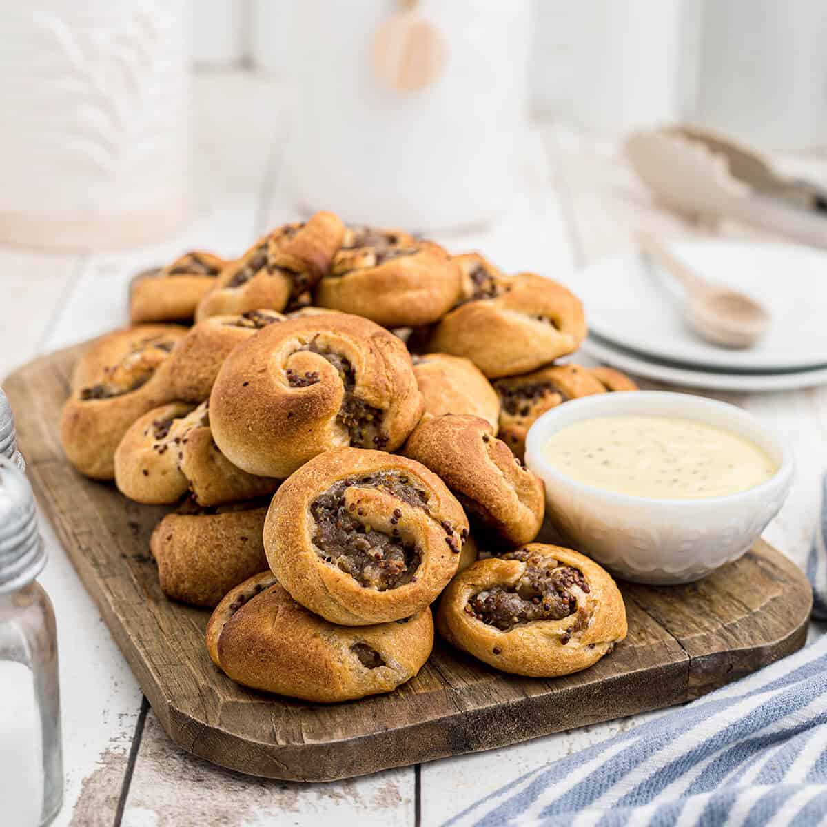 Finished sausage swirls on a board with dipping sauce.