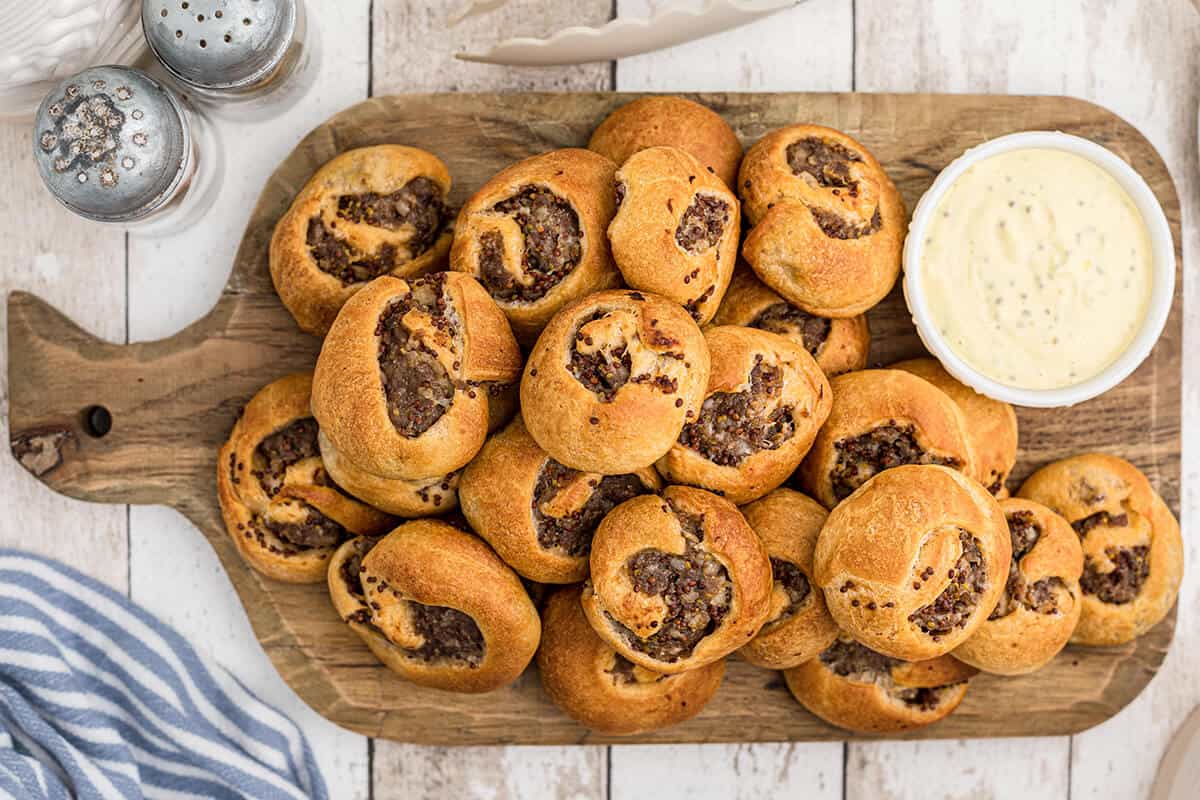 Finished sausage swirls on a board with dipping sauce.