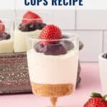 A no-bake cheesecake cup topped with berries and sauce, with strawberries and a spoon nearby.