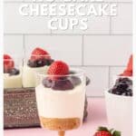 A no-bake cheesecake cup topped with strawberries and cherries sits on a table with more desserts nearby.