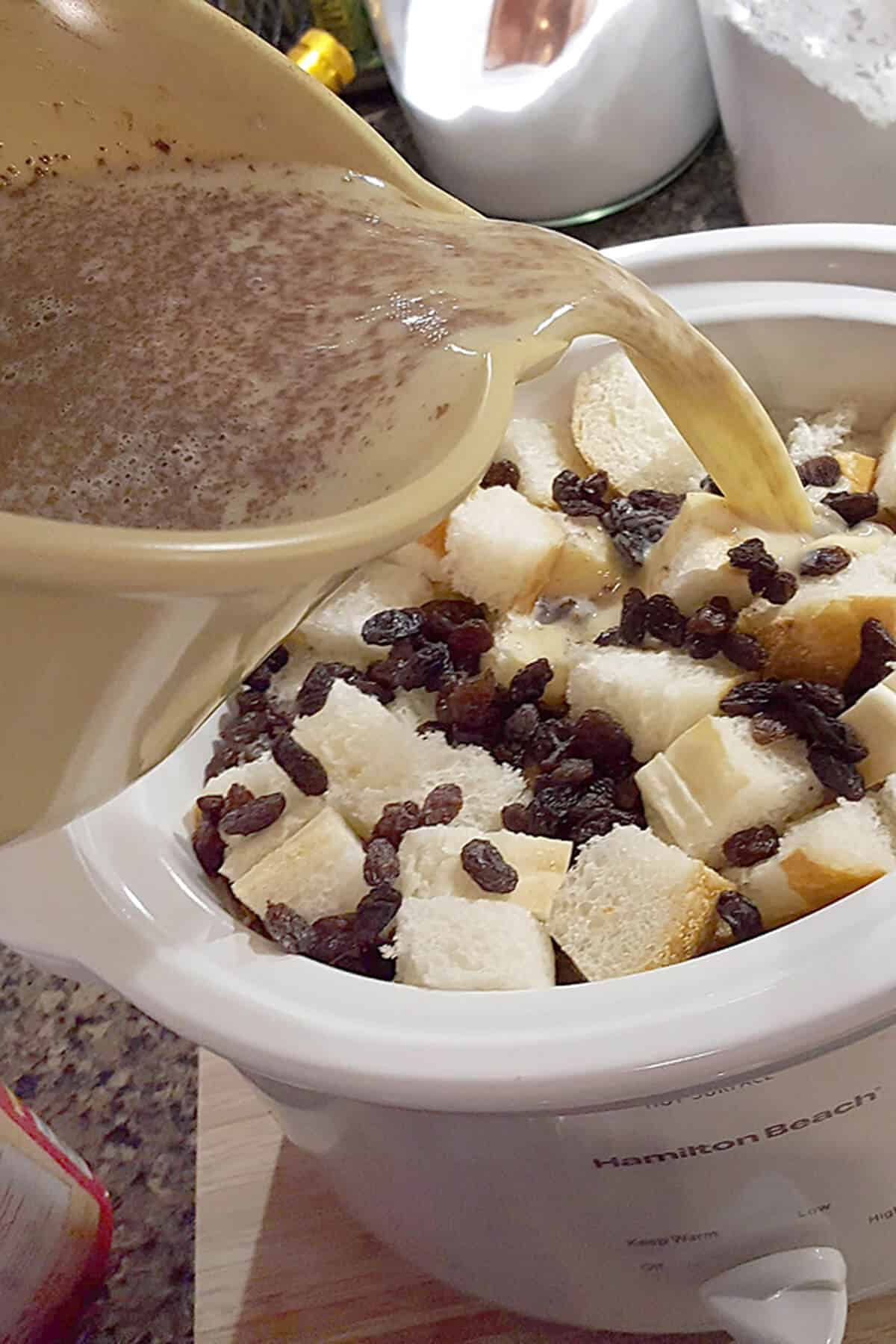 Pouring custard mixture over bread cubes and raisins.