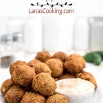 Finished hush puppies on a plate with dipping sauce on the side.