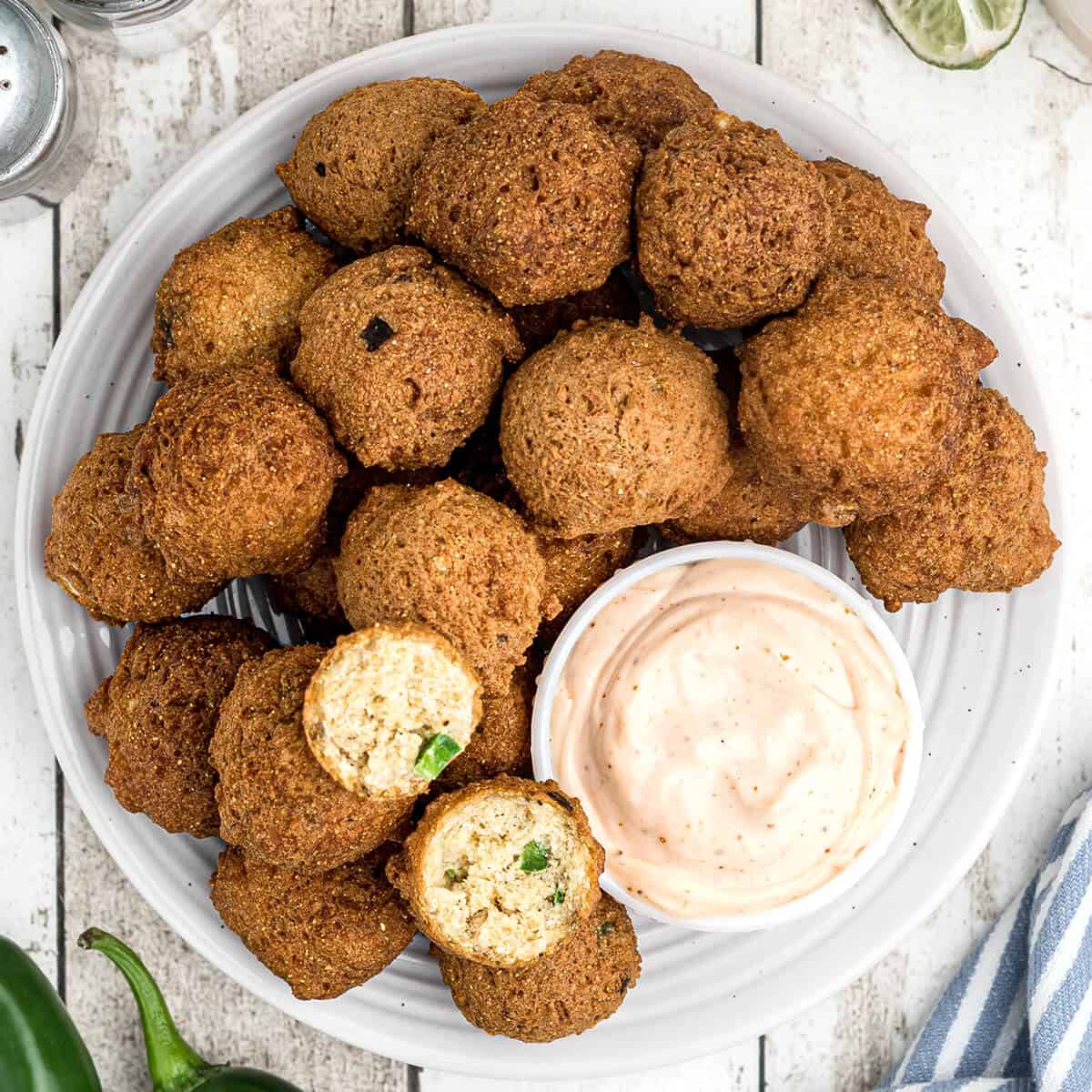 Finished hush puppies on a plate with dipping sauce on the side.