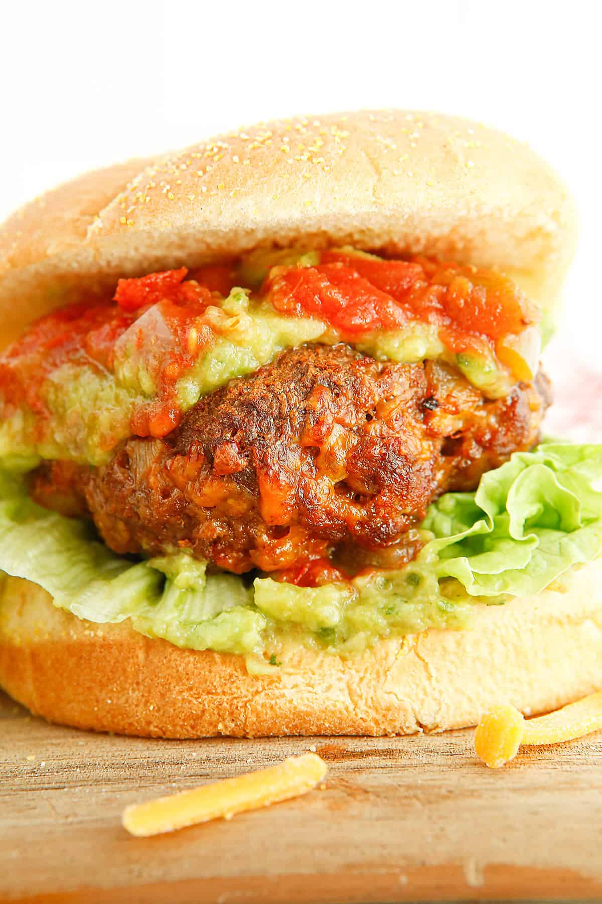 A close-up of a burger with lettuce, guacamole, salsa, and a thick patty on a sandwich bun.