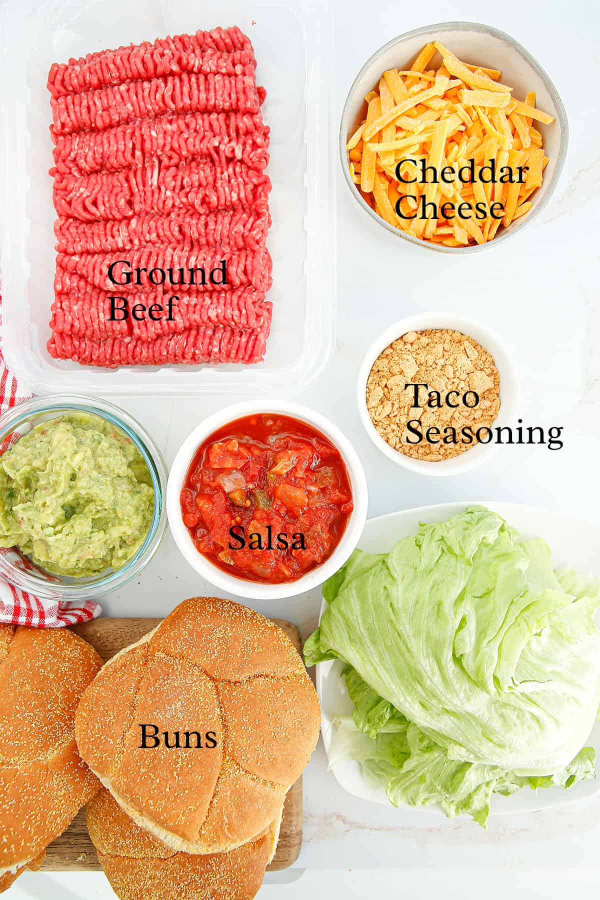 Top view of taco burger ingredients: ground beef, cheddar cheese, taco seasoning, salsa, guacamole, lettuce, and buns.
