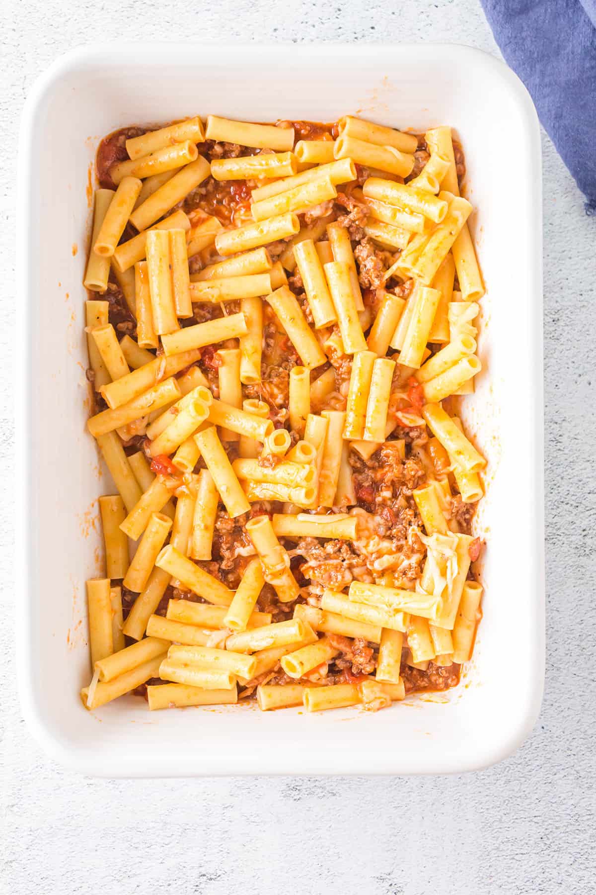 Ziti, meat sauce, and cheese mixture in a baking dish.
