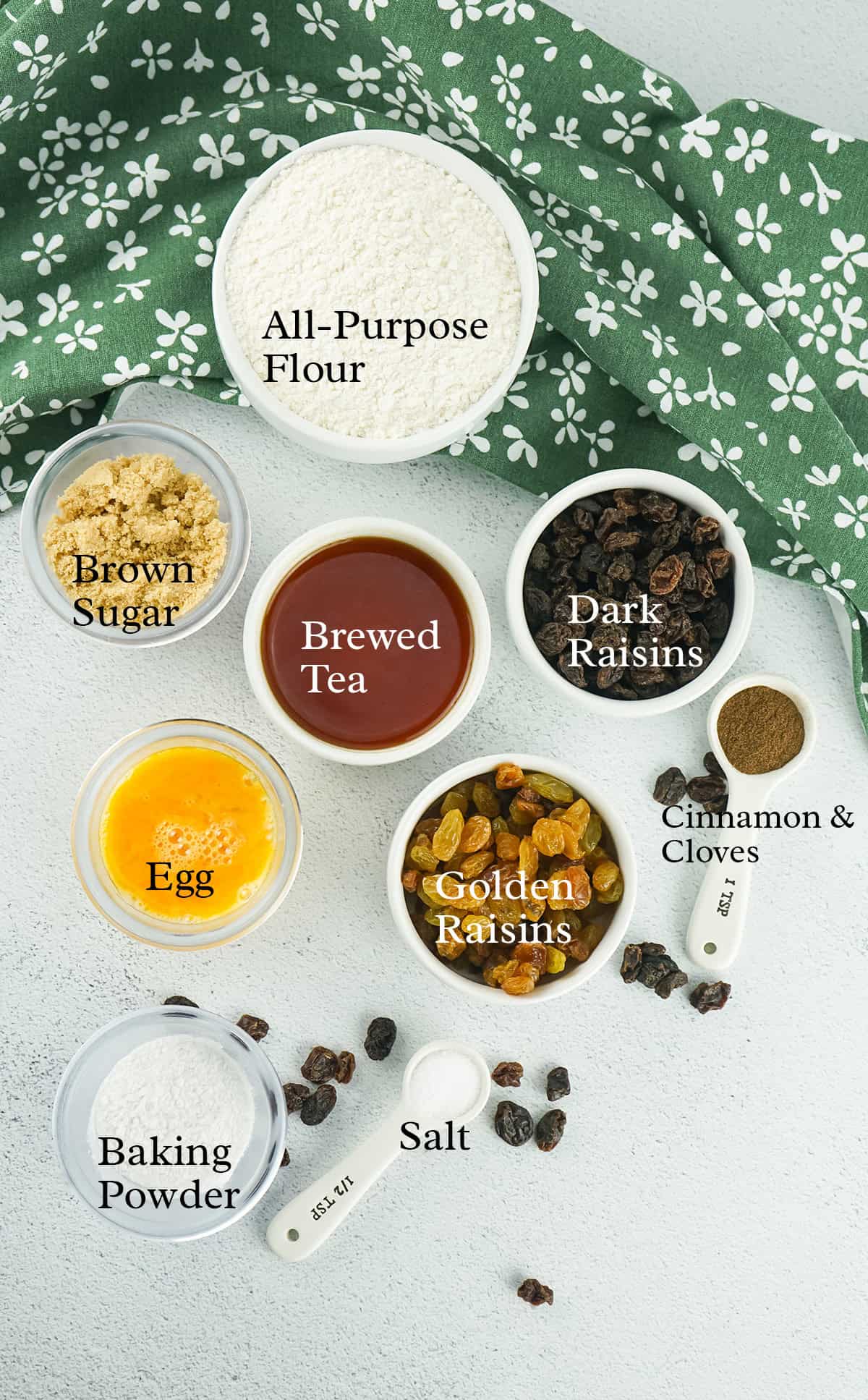 Top-down view of baking ingredients in bowls: flour, brown sugar, brewed tea, raisins, egg, spices, baking powder, and salt.