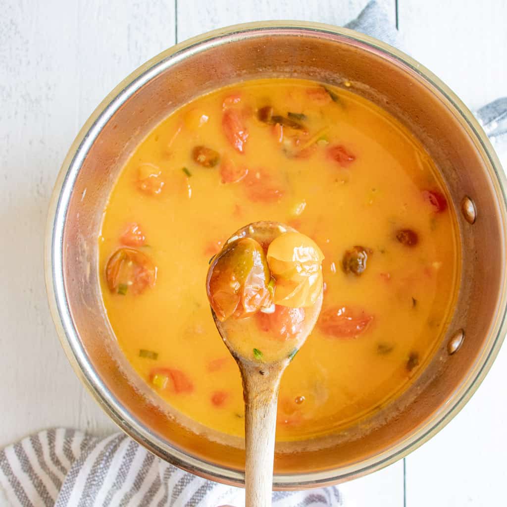 A wooden spoon holds chunky tomato sauce above a pot, next to a striped kitchen towel on a white table.