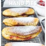 Three golden-brown fried cherry hand pies dusted with powdered sugar on a cooling rack.