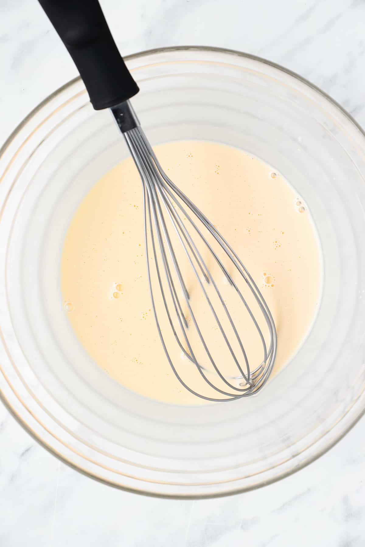 Cream, eggs, and vanilla whisked together in a bowl.
