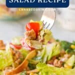 A fork holds up a bite of turkey taco salad with lettuce, tomato, and corn. Text reads Turkey Taco Salad Recipe.