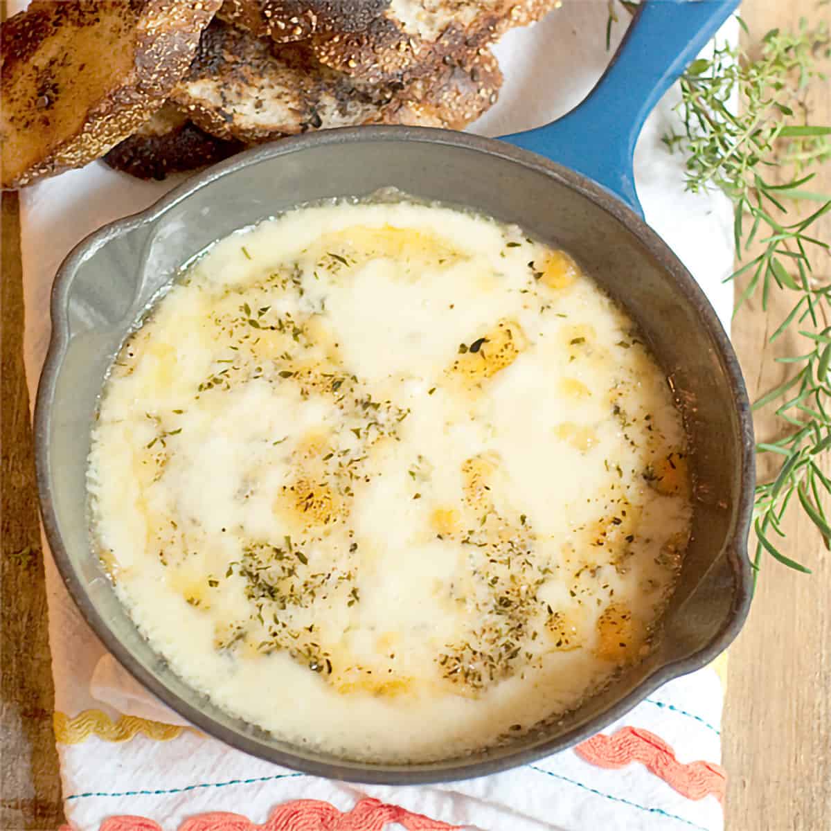 Baked fontina and herbs in a small blue skillet.