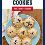 A blue plate with seven blueberry pie cookies drizzled with icing, on a wooden table.