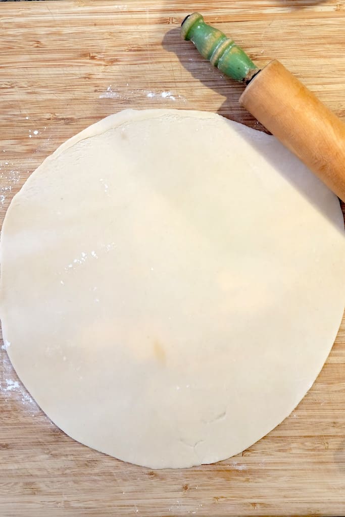 A rolled-out dough circle on a wooden board with a rolling pin beside it.
