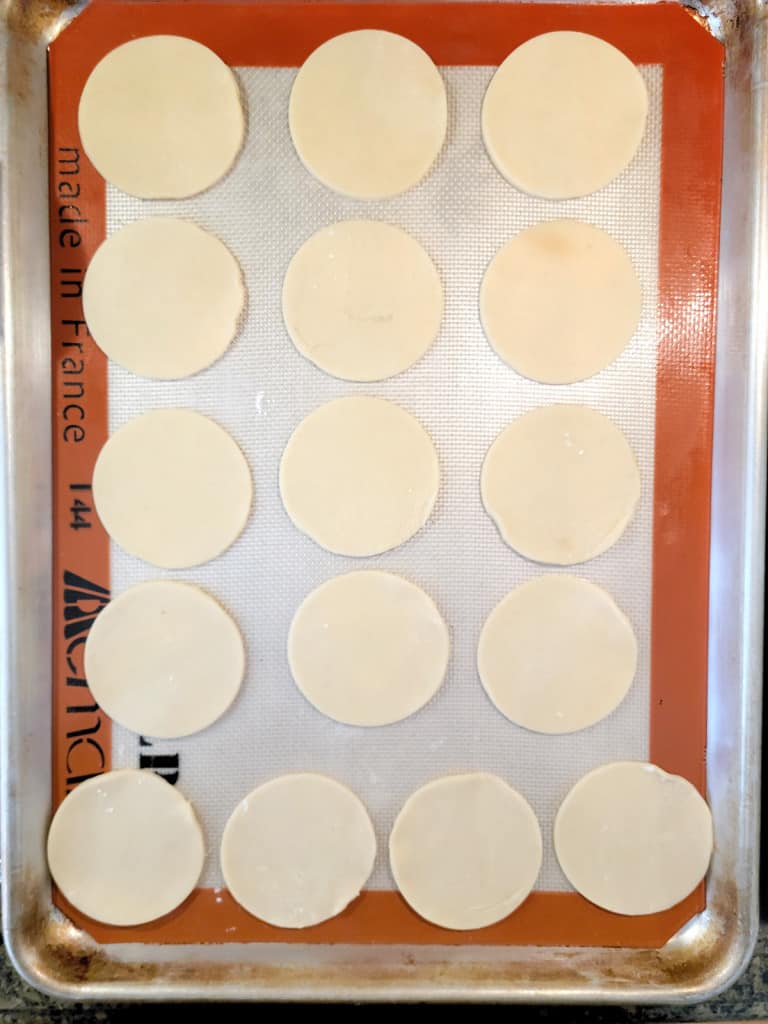 Baking sheet with 16 round dough circles evenly spaced on a silicone baking mat.