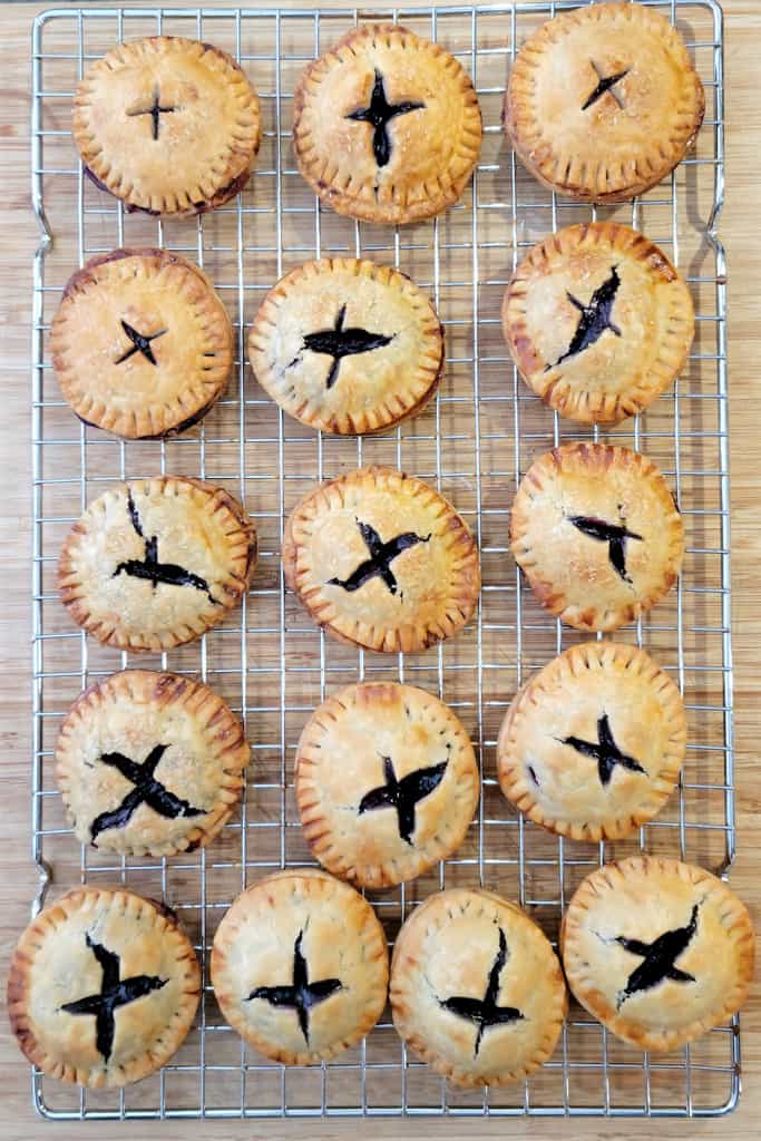 Eighteen golden pie cookies with crimped edges and X-shaped vents, cooling on a wire rack.