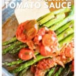 Roasted asparagus topped with burst cherry tomato sauce on a baking sheet, with a spatula beside it.