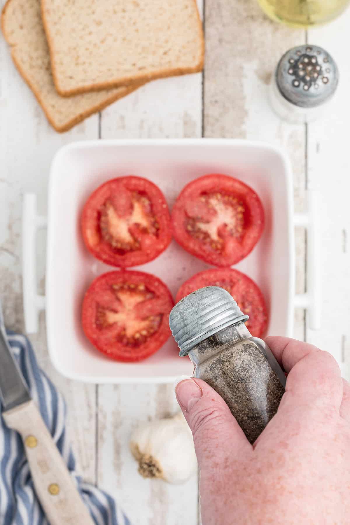 Adding salt and pepper to each tomato half.