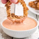 Comeback sauce in a white bowl with an onion ring being dipped.