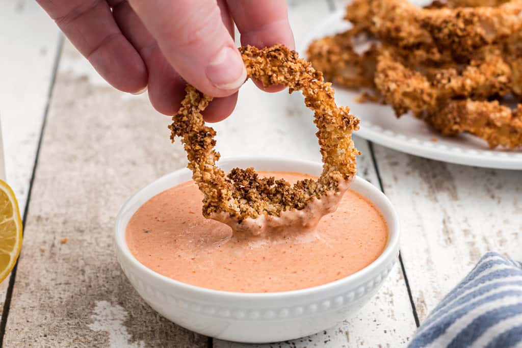 Onion ring being dipped into comeback sauce.