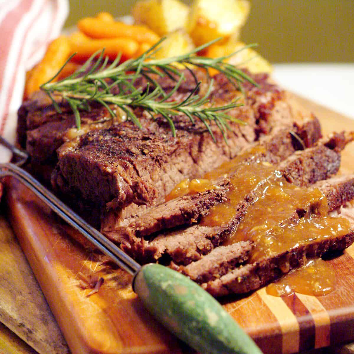 Sliced pot roast with gravy on a wooden board.