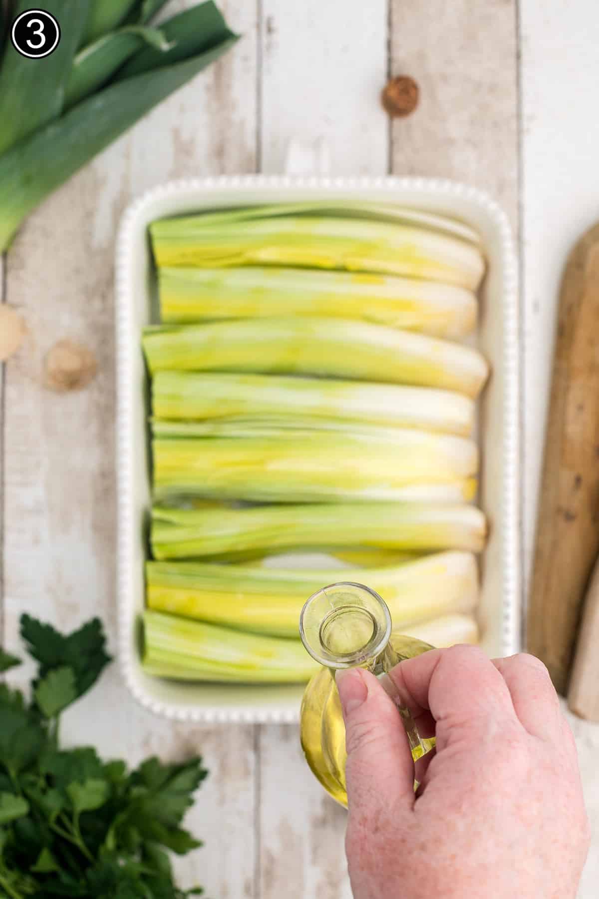 Drizzling olive oil over leeks in a baking dish.