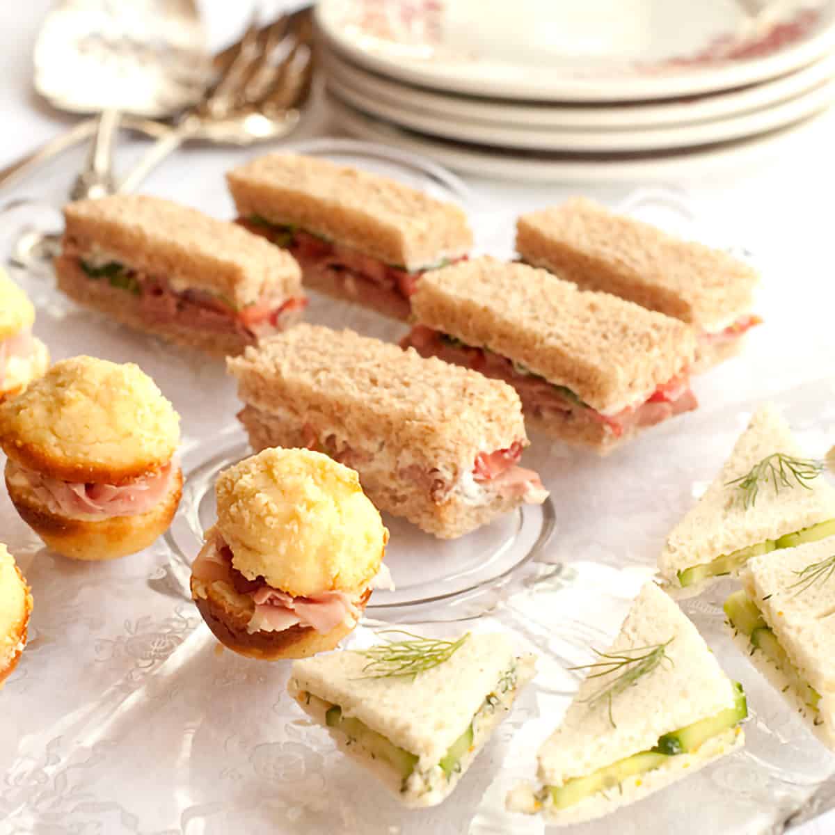 Three types of tea sandwiches on a glass tray.
