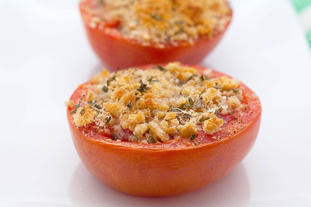 Two baked tomatoes provencal on a white plate.