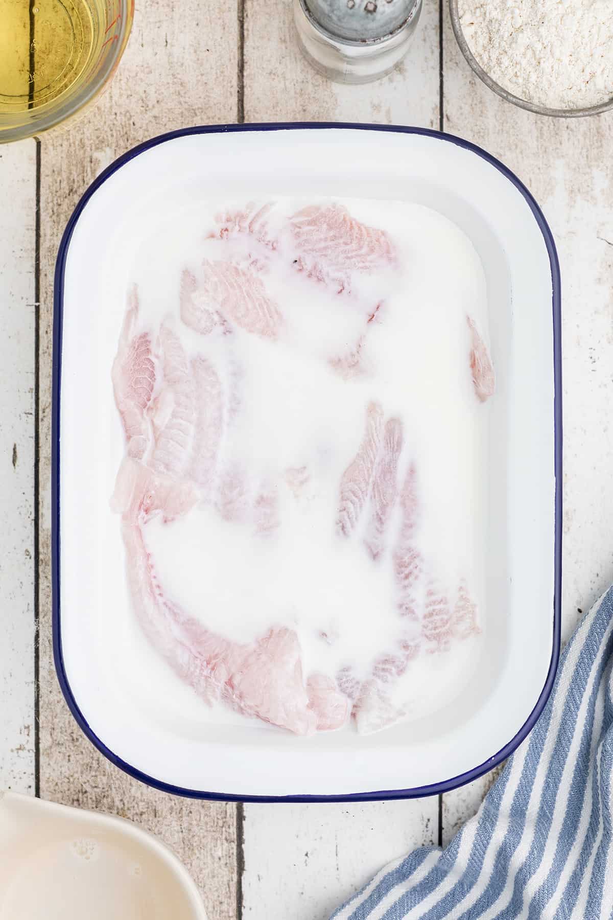 Catfish fillets covered with milk in a pan.