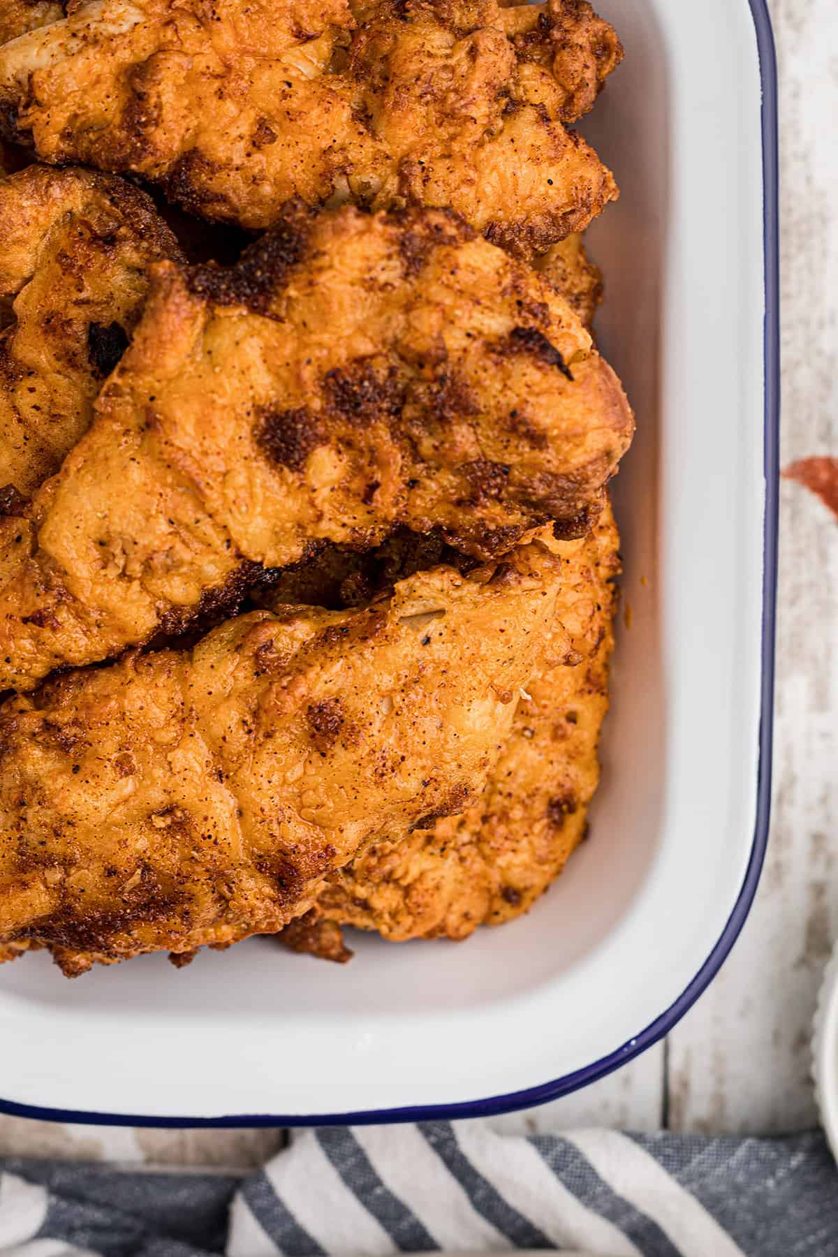Golden fried chicken pieces stacked in a white enamel tray with a blue rim.