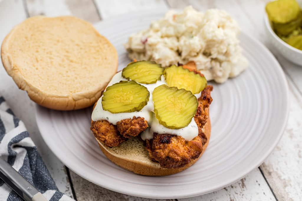 A hot chicken sandwich being assembled on a white plate.
