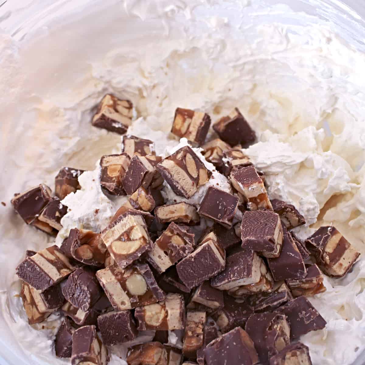 Chopped candy bars being folded into cream cheese mixture.