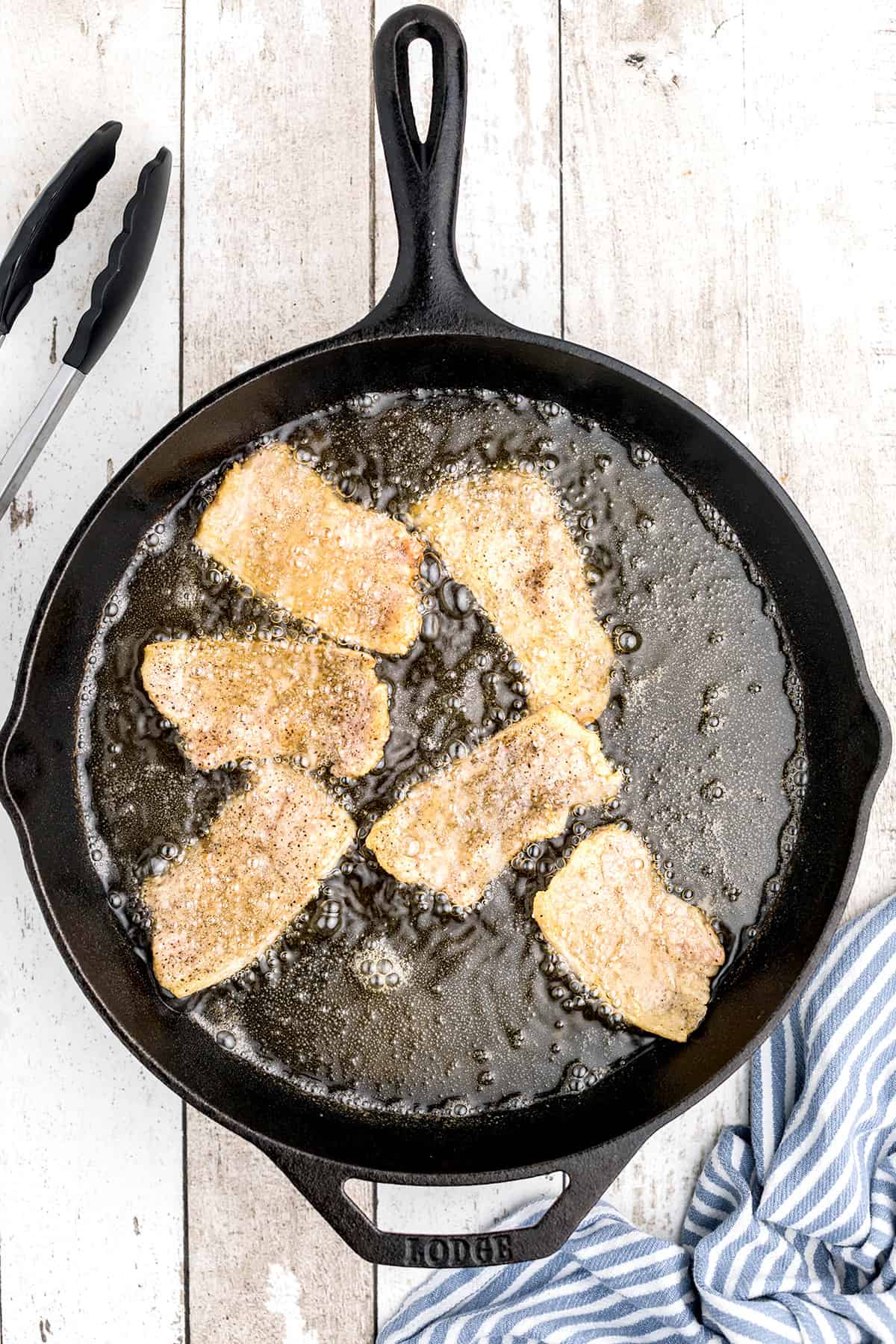 Pork pieces frying in a skillet.