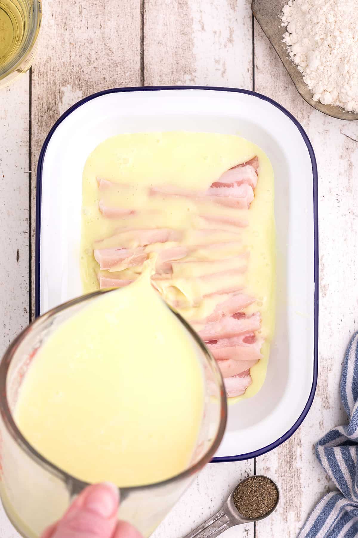 Slices of salt pork soaking in a pan covered in buttermilk.