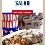 Grilled steak salad with blue cheese, onions, and greens on a white plate; patriotic utensils in background.