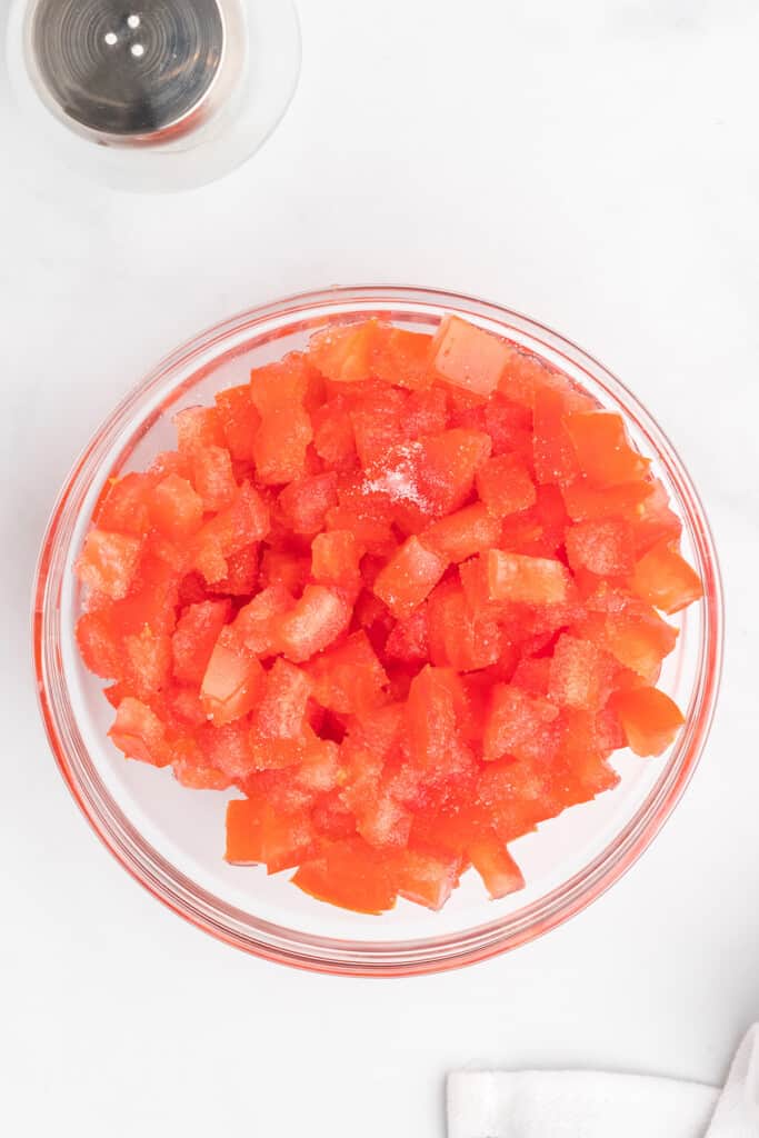 A glass bowl filled with diced tomatoes on a white surface.